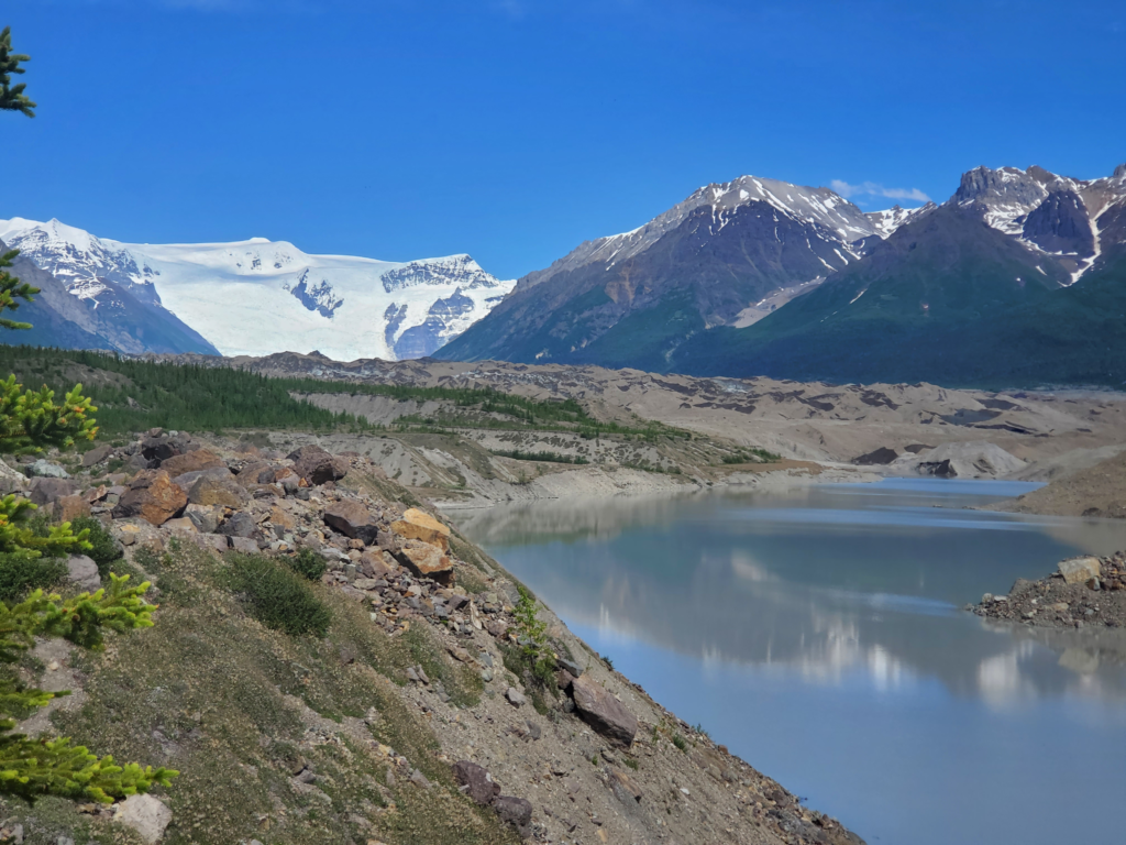 End of the trail. Meltwater in the foreground, rock covered glacier behind, icefield and massive icefalls in distance.