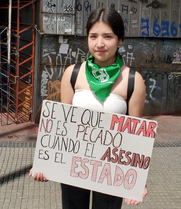Demonstrator, Santiago, Chile, 25 Oct 2019. Hr sign says, "Apparently killing is not a sin if the state is the killer."